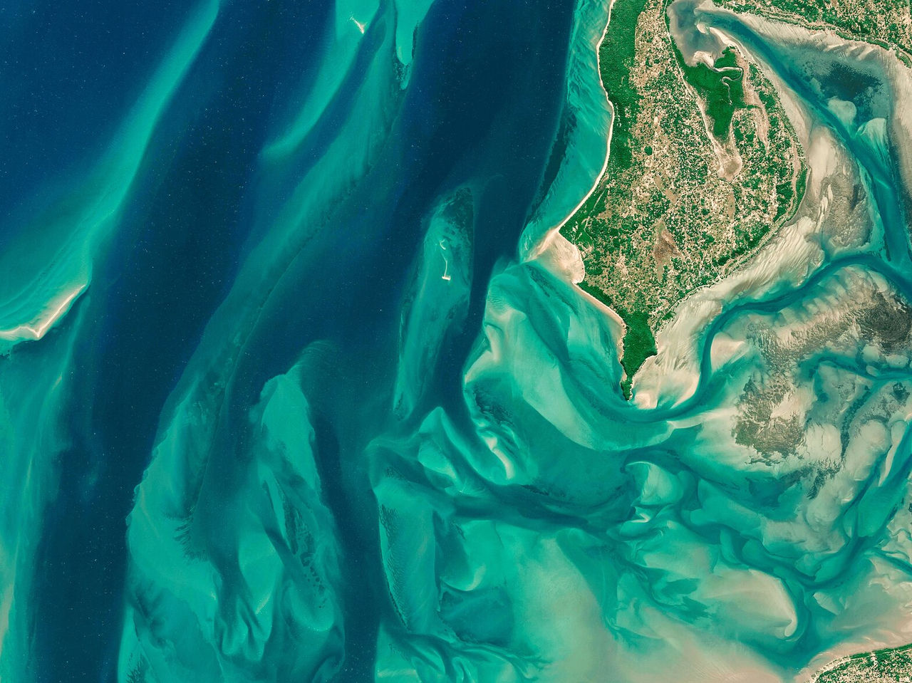 Vista aérea sobre llanuras verdes y el océano, creando un patrón asimétrico de arena y agua