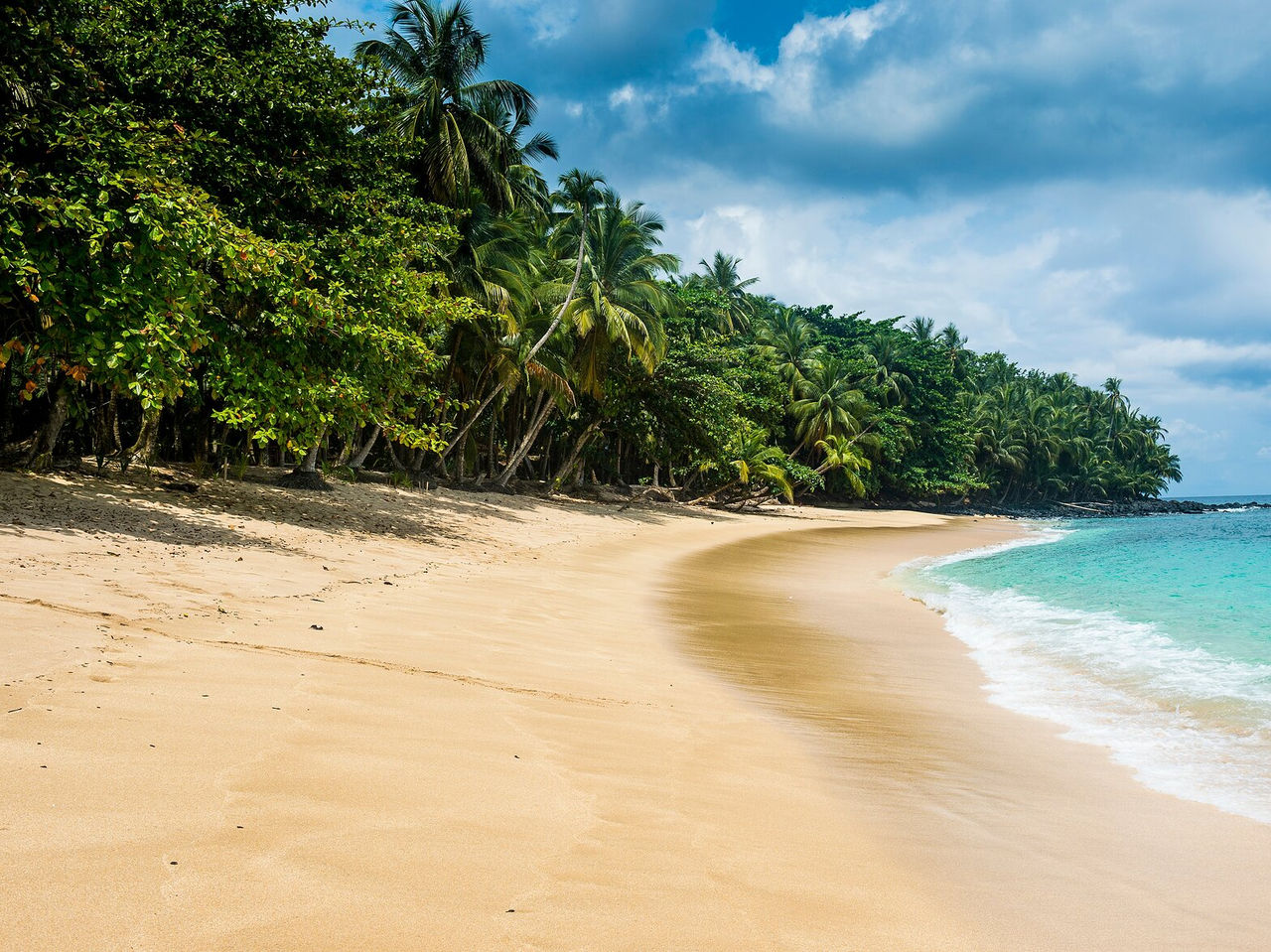 Playa desierta en São Tomé, con un mar muy azul y tranquilo, y una vegetación densa rodeando la playa