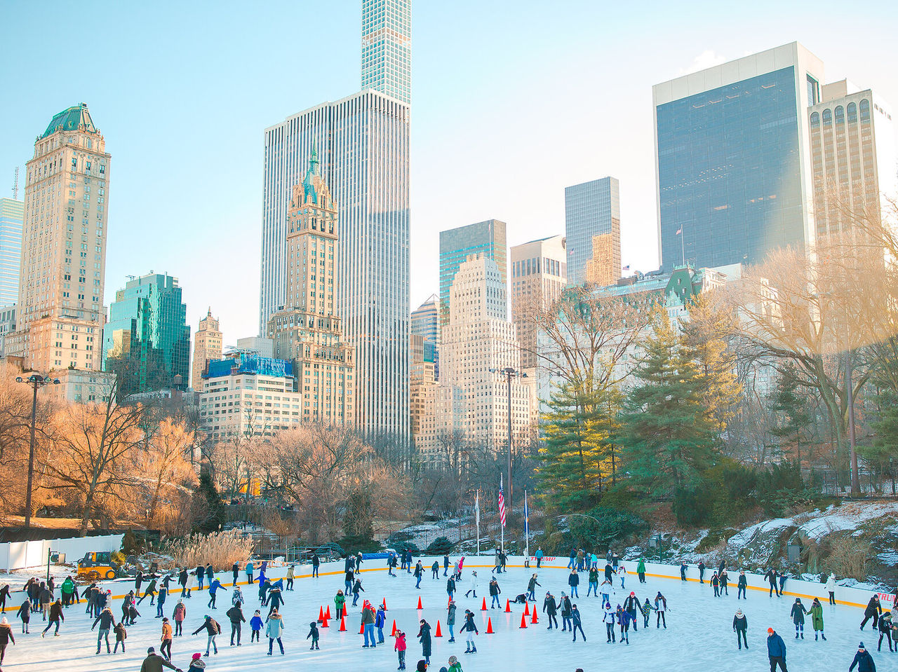 Personas patinando sobre hielo en Central Park, con el horizonte de la ciudad al fondo