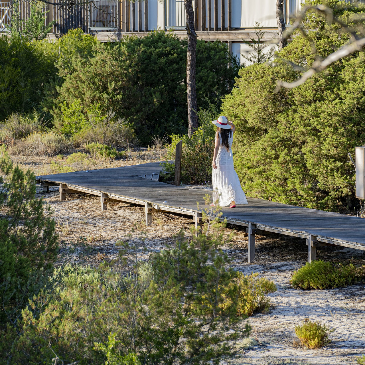 Pasadizo de madera en el Pestana Tróia Eco Resort, donde una mujer con vestido y sombrero pasea entre las villas