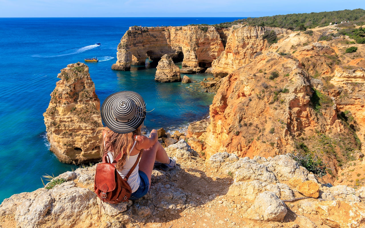 Mujer admirando la vista panorámica de la costa del Algarve, con aguas cristalinas y un acantilado rodeado de vegetación