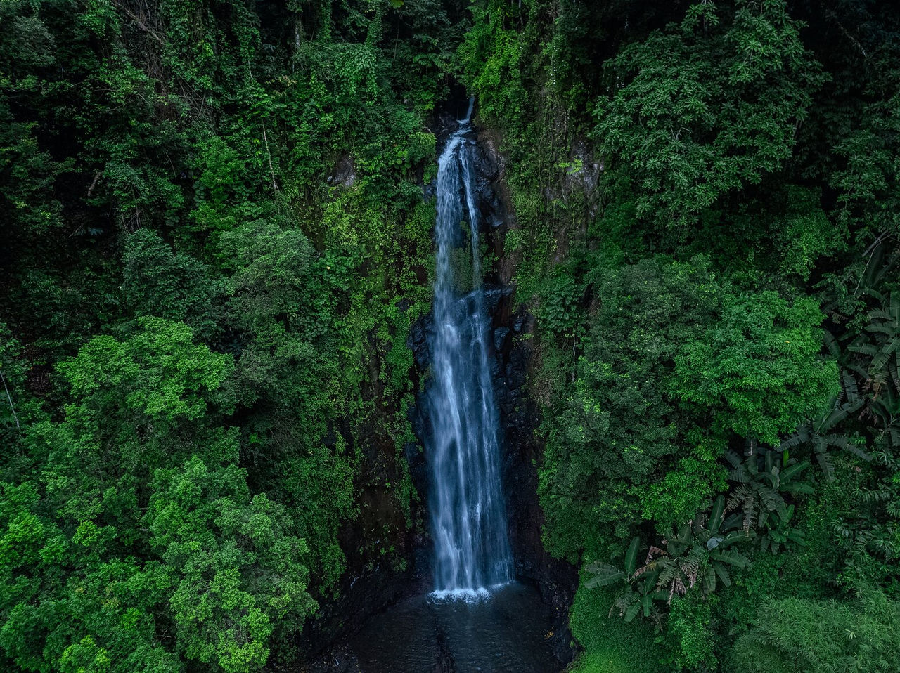 Cascata comprida no meio de densa vegetação, que desagua num pequeno lago em São Tomé 