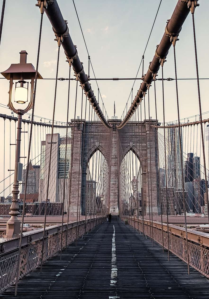 Vista panorâmica da ponte do Brooklyn, com seus cabos de aço e estrutura de ferro, sob um céu azul claro