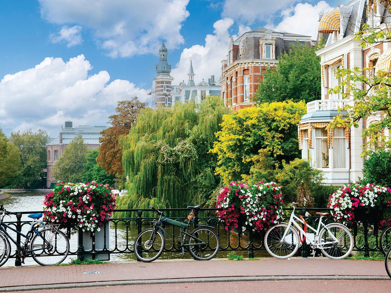 Ponte sobre um canal em Amsterdão, com bicicletas estacionadas, flores coloridas e os típicos edifícios por trás