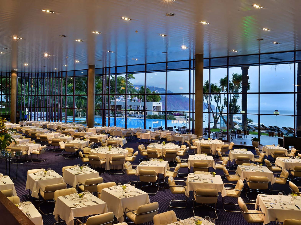 O restaurante Panorâmico, do Hotel no Funchal, na Ilha da Madeira, tem várias mesas e cadeiras almofadadas em bege