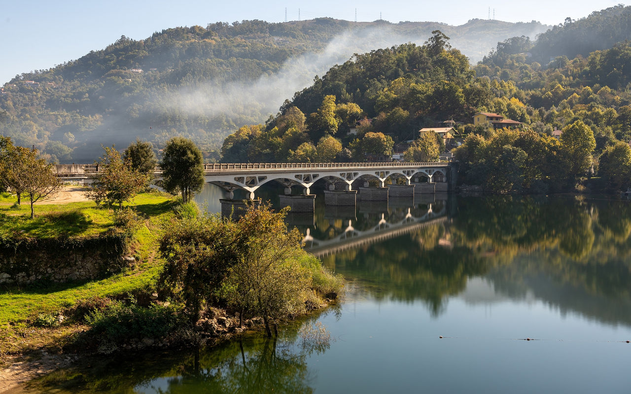 Paisagem do norte de Portugal com uma ponte de pedra sobre um rio, cercada por colinas verde
