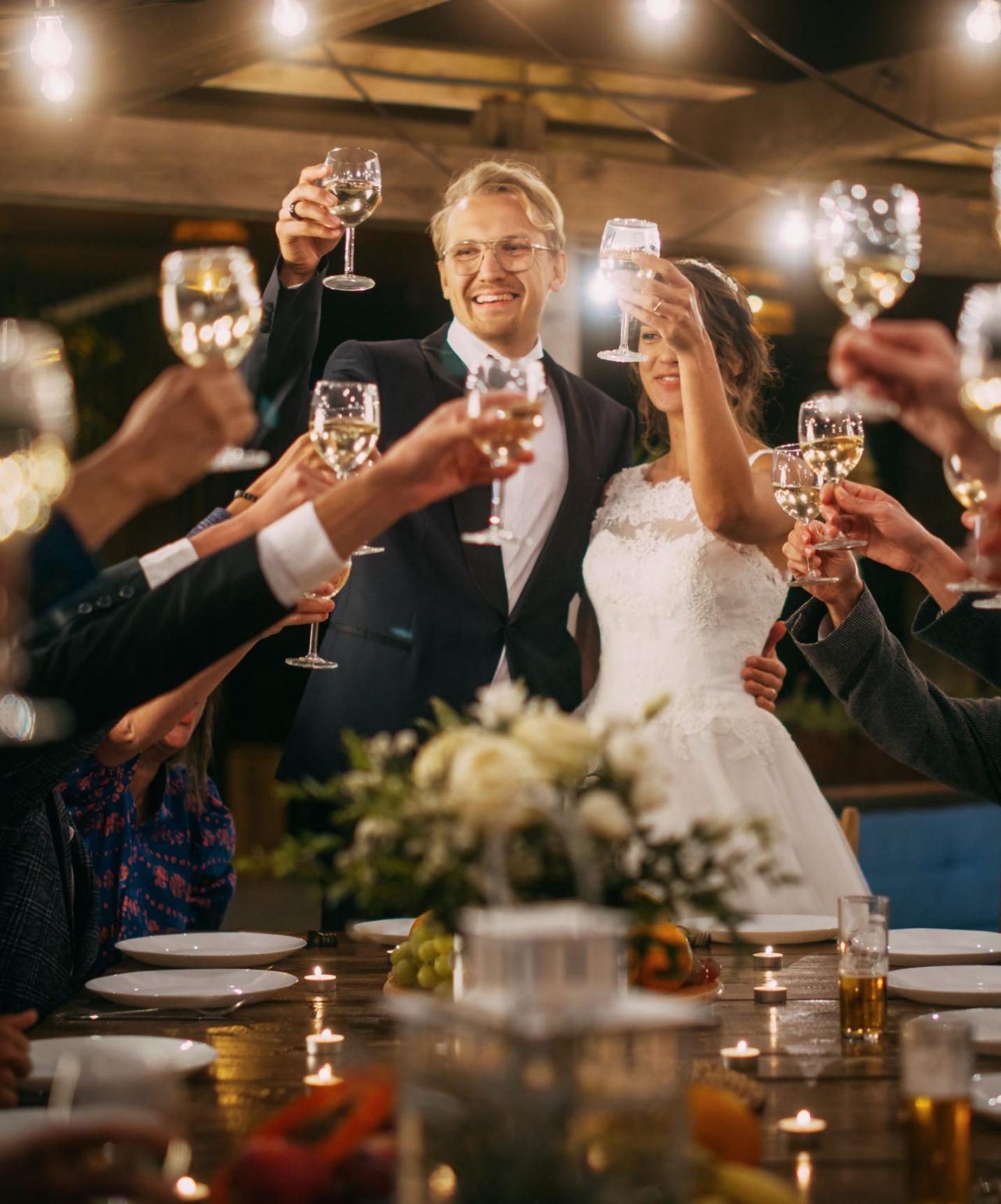 Noivos celebram o seu casamento, brindando com os seus convidados numa mesa elegante com arranjo de flores