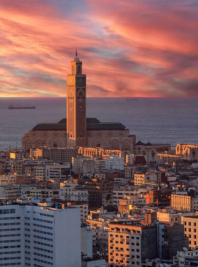 Aerial view over Casablanca, with the sunset illuminating various buildings, the sky over the sea, and the tower