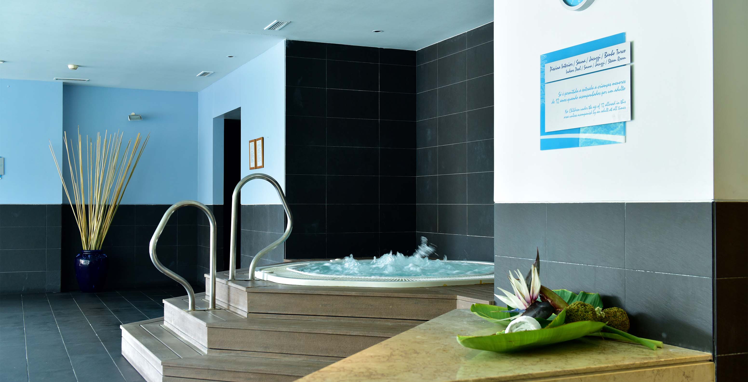 Jacuzzi with wooden steps and metal supports with black stone floor and wall clock