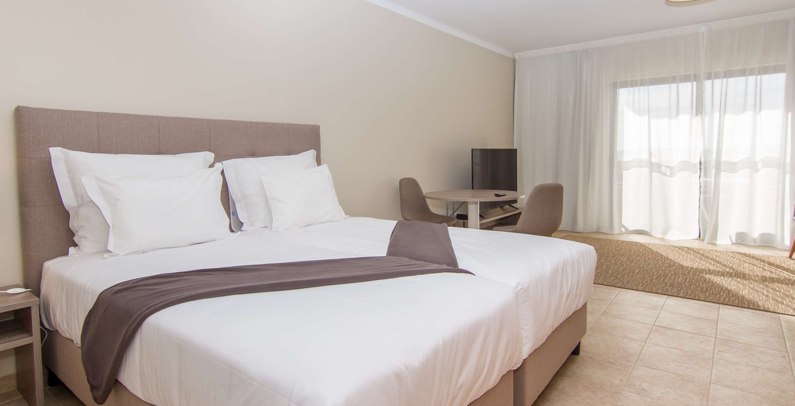The Studio at Pestana Gramacho Residences features two single beds, a table with two chairs, and a window