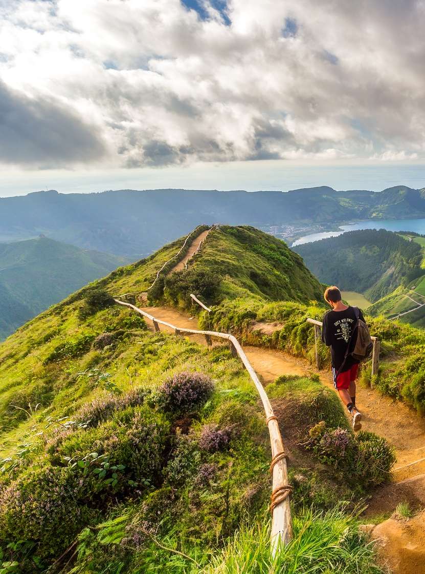 Man walks on a dirt trail with a view of Sete Cidades Lagoon, São Miguel Island, Azores