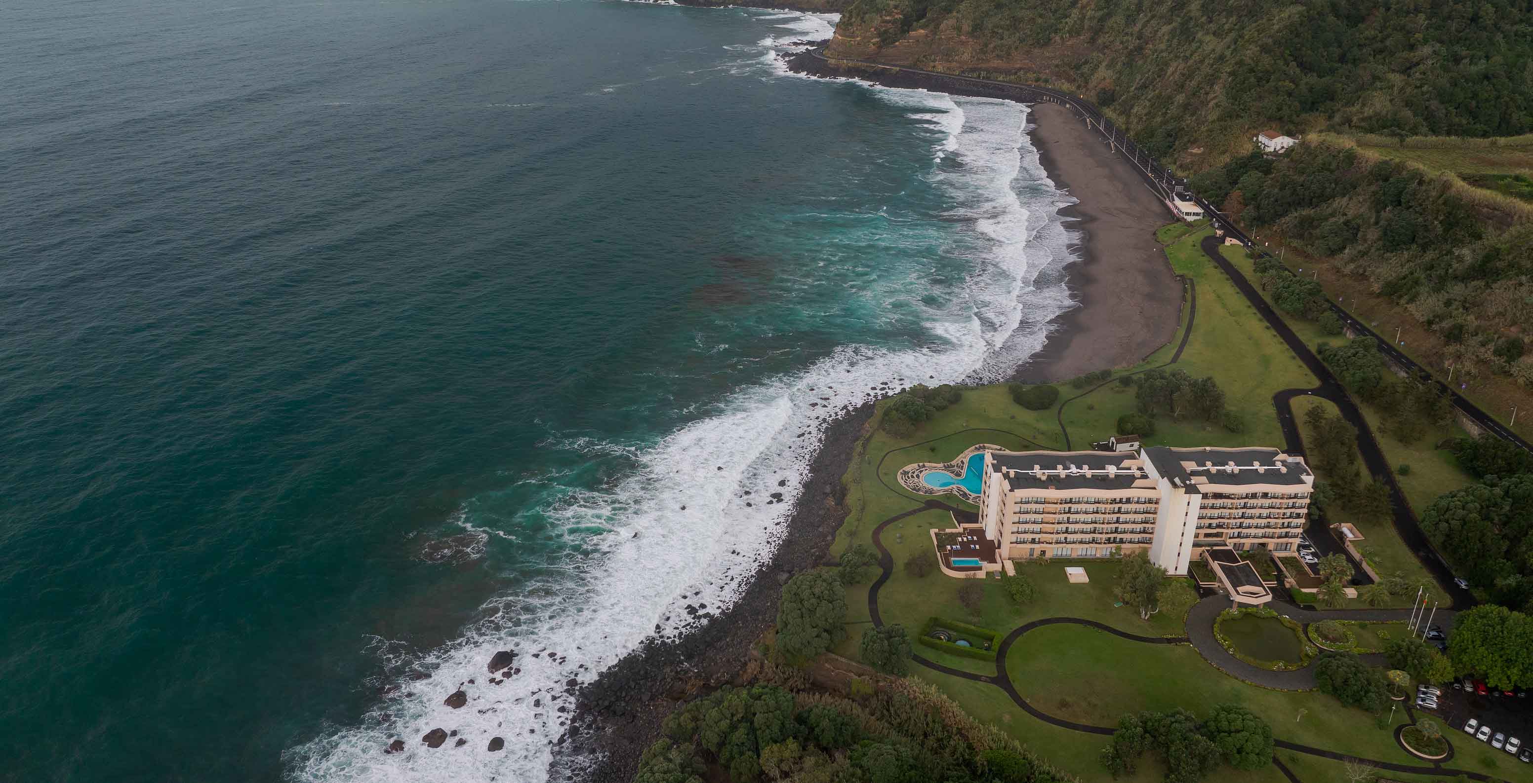 Aerial view of Pestana Bahia Praia by the coast with beach, waves, and green vegetation around