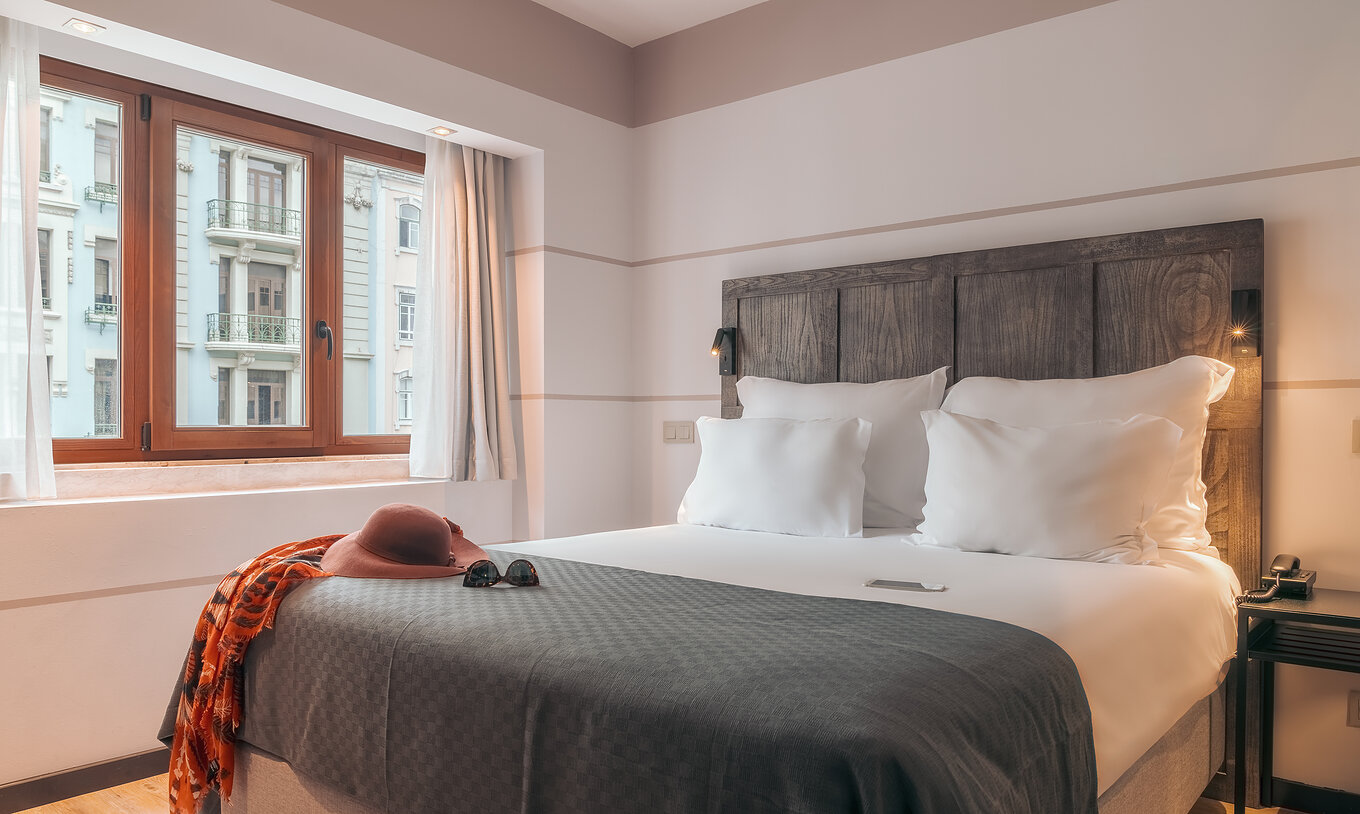 The Double Classic Room at Pestana Lisboa Vintage has a double bed with headboard and gray blanket and a wooden window