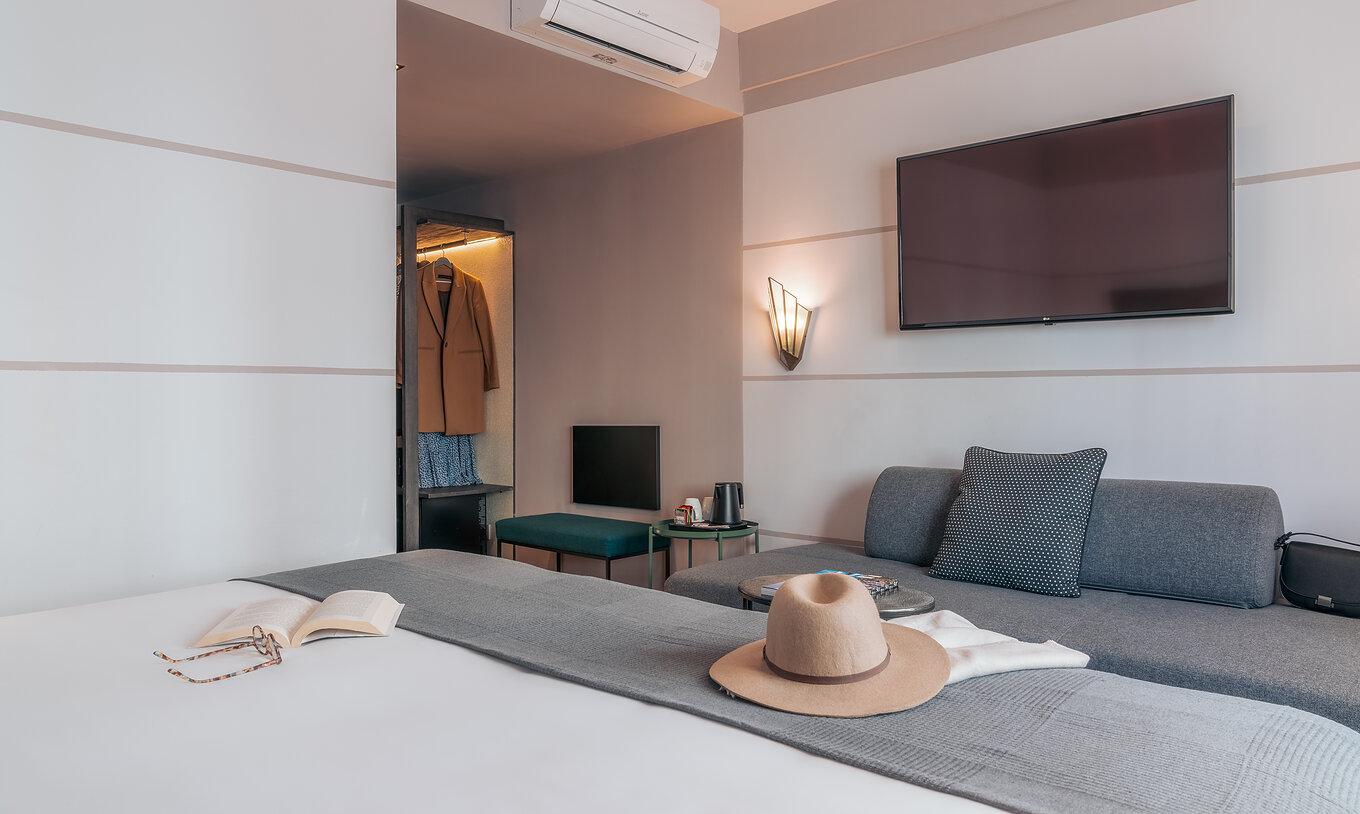 The Double Classic Room at Pestana Lisboa Vintage has a double bed with gray blanket, gray sofa and a TV