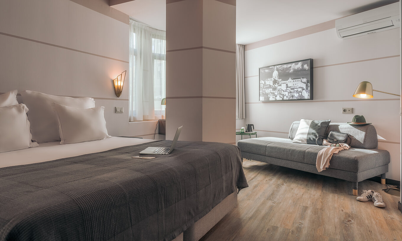 The Double Superior Room at Pestana Lisboa Vintage has a double bed with gray blanket, gray sofa and white sneakers