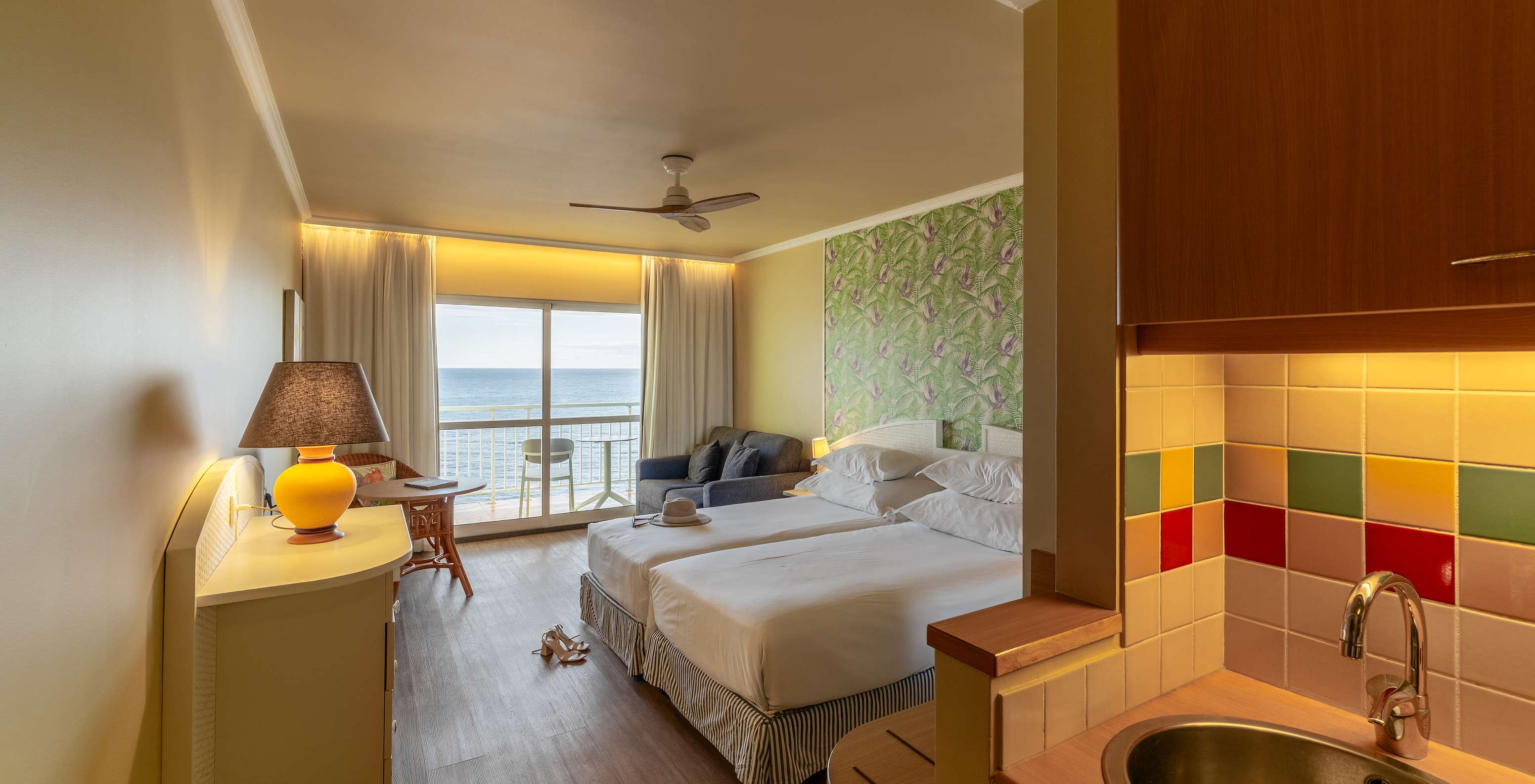 The Pestana Ocean Bay All Inclusive Premium Sea View has a double bed, palm tree wallpaper, a sofa, and a balcony