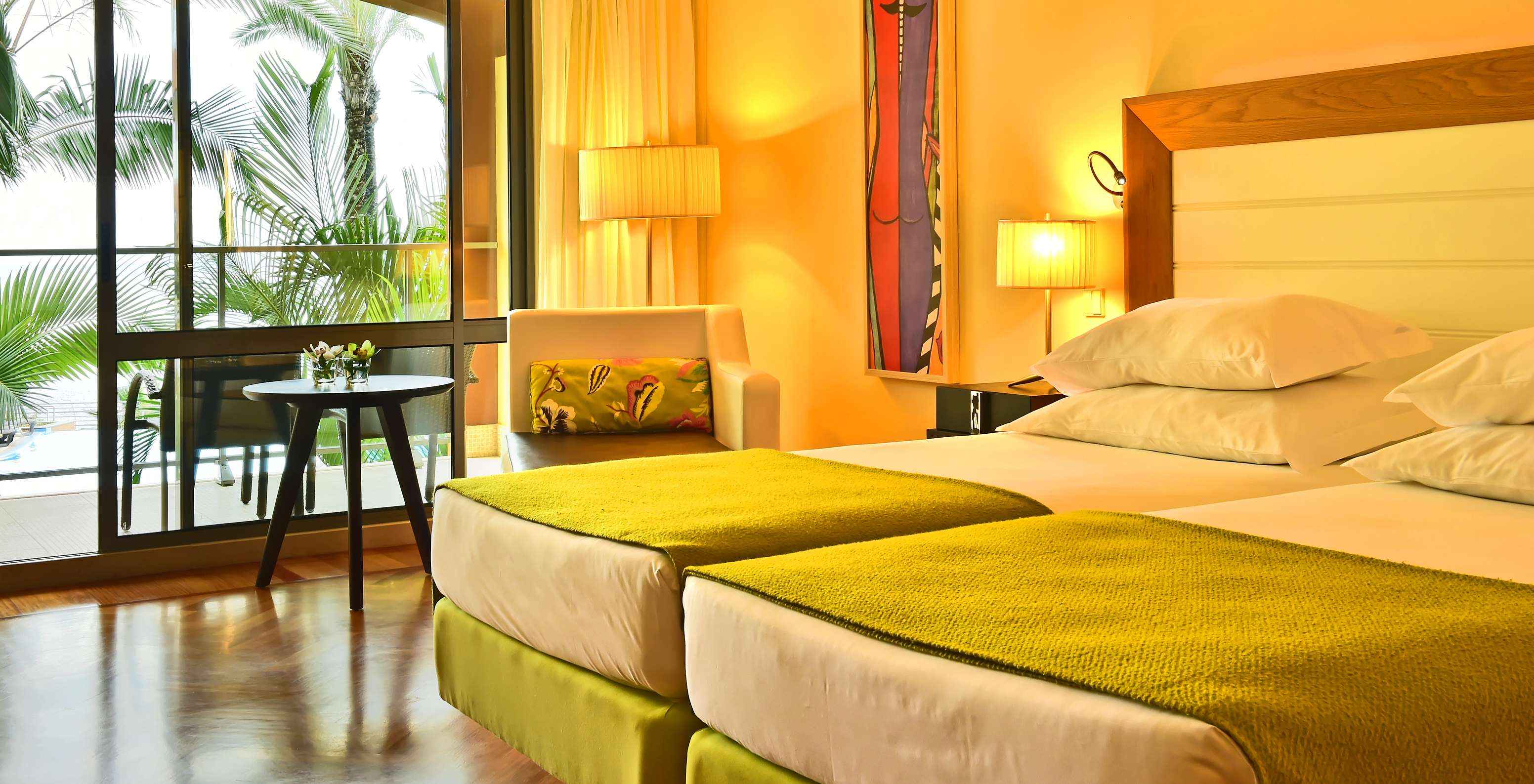 The Classic Pool View of Pestana Promenade has two beds with a green bedspread and a large window to the balcony