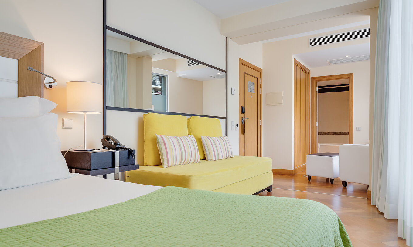The Classic Twin of Pestana Promenade has a double bed, a yellow sofa, and a large mirror on the wall