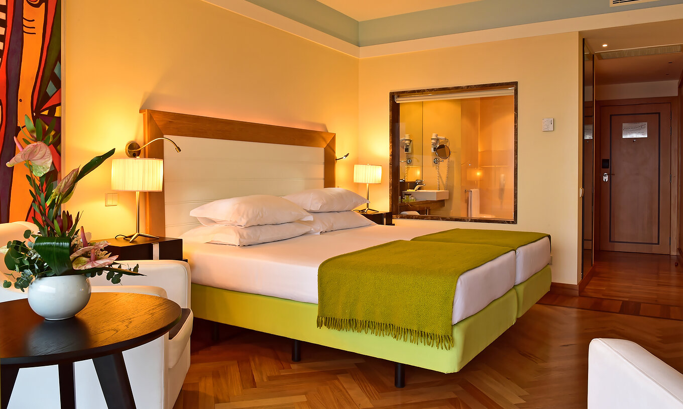 The Superior of Pestana Promenade has a bed with a green bedspread and a glass to the bathroom at the back