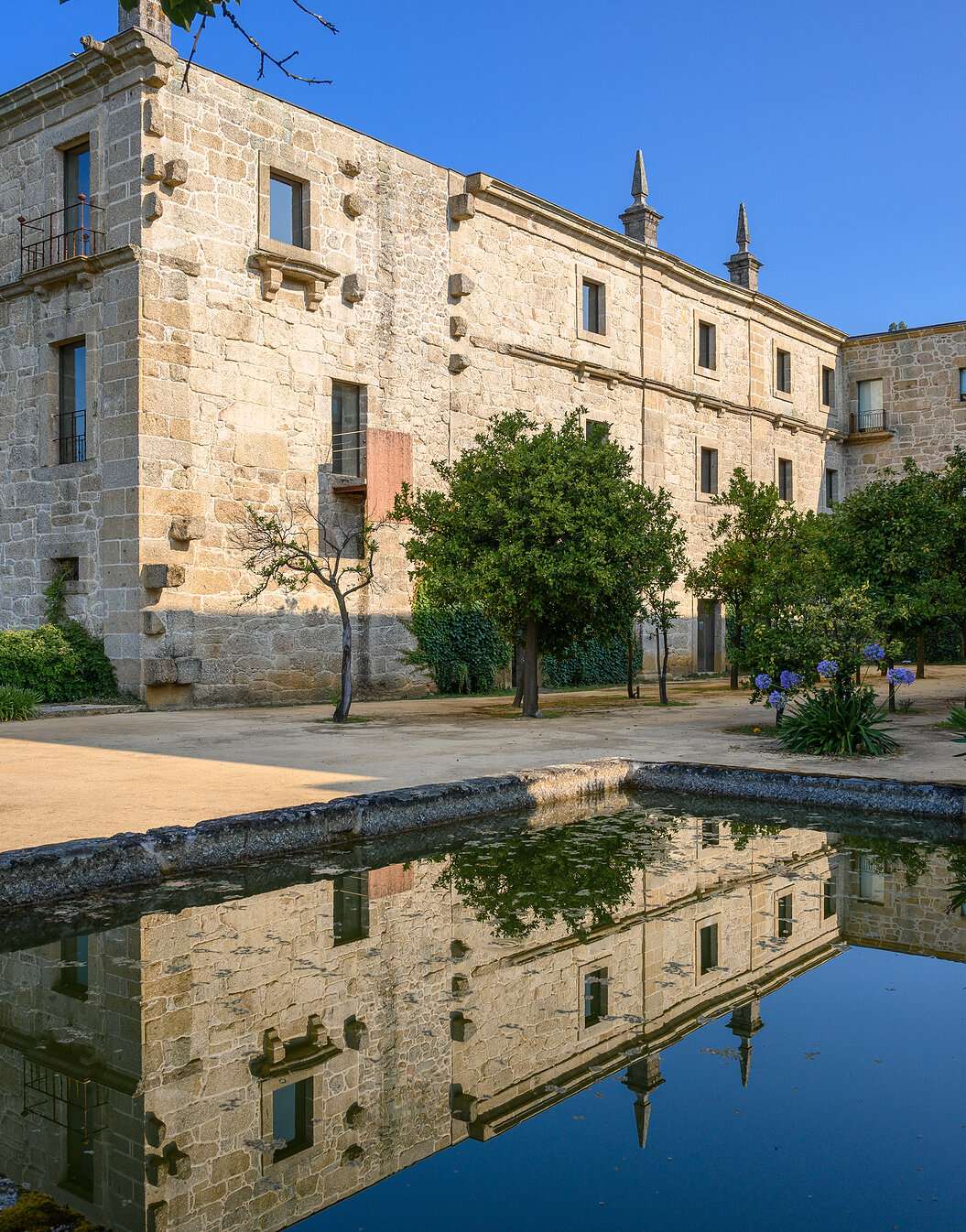 Exterior view of the building of Pousada Mosteiro Amares, a historic hotel in Gerês, made of stone with a lake in front