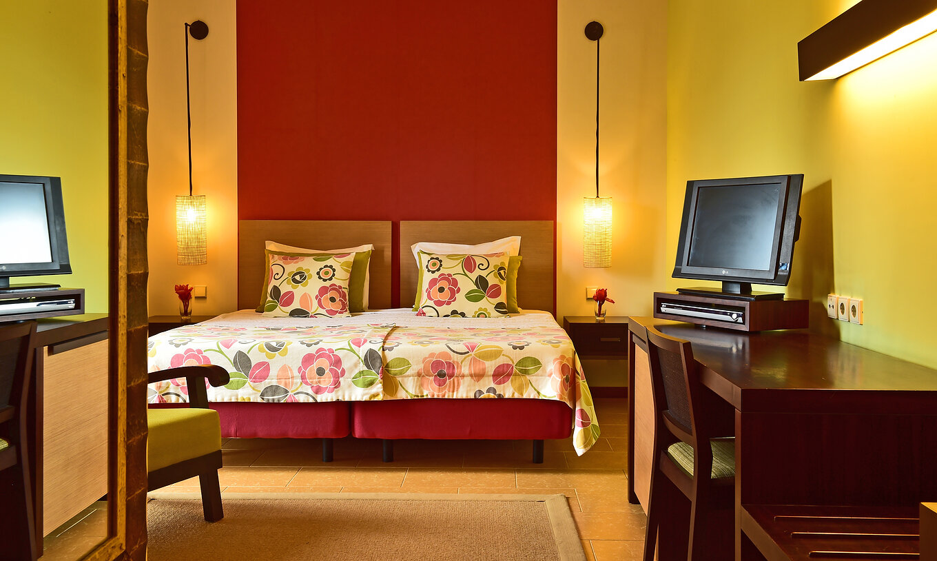 The Standard Room of Pestana São Tomé is a spacious room with two single beds, an armchair, and a desk with TV