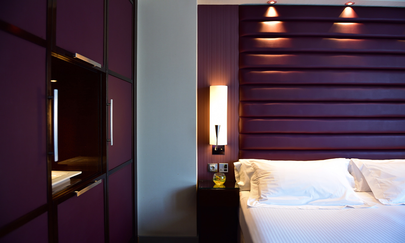 Standard room at Pestana Arena Barcelona has modern decor in purple tones, a double bed and a wardrobe