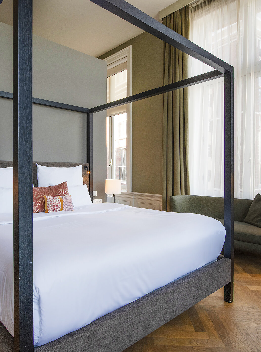 Junior Suite - River View at Pestana Amsterdam Riverside has a double bed with canopy and a green sofa