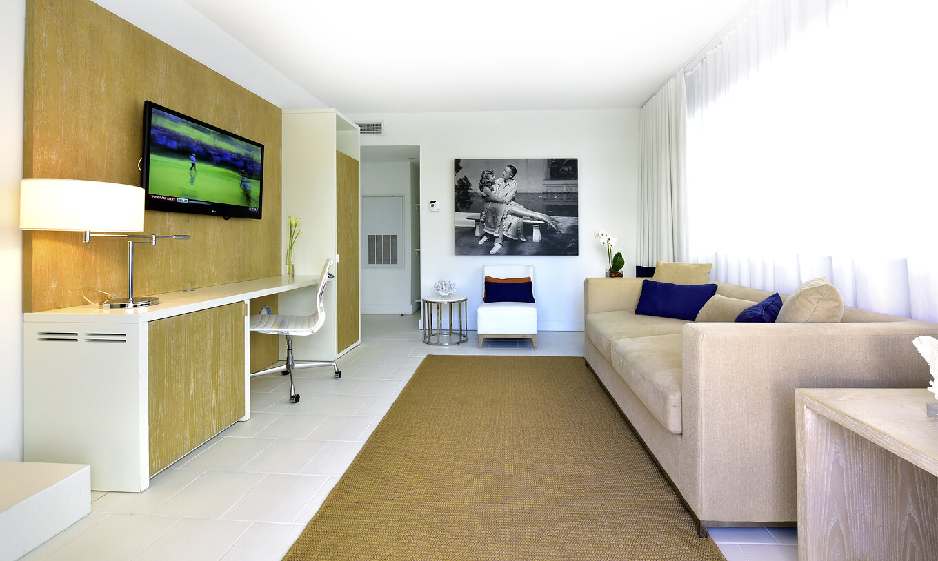 The Two Bedroom Suite with Balcony at Pestana Miami South Beach has a living room with sofa, chair, TV and a desk