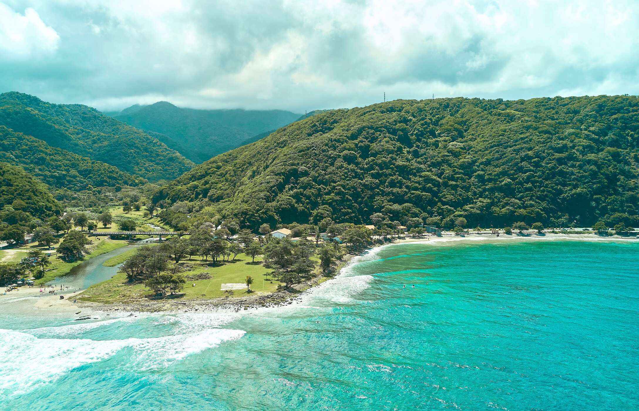 Aerial view of La Punta Beach in Venezuela, with crystal-clear waters, surrounded by green mountains.