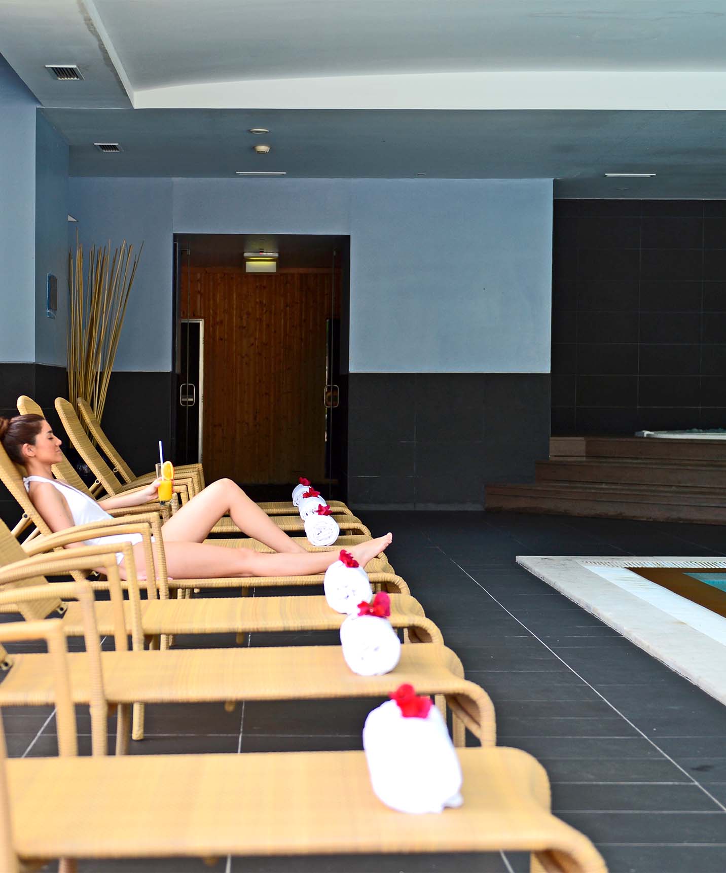 Piscina interior con escaleras metálicas y jacuzzi, con tumbonas y una mujer tumbada