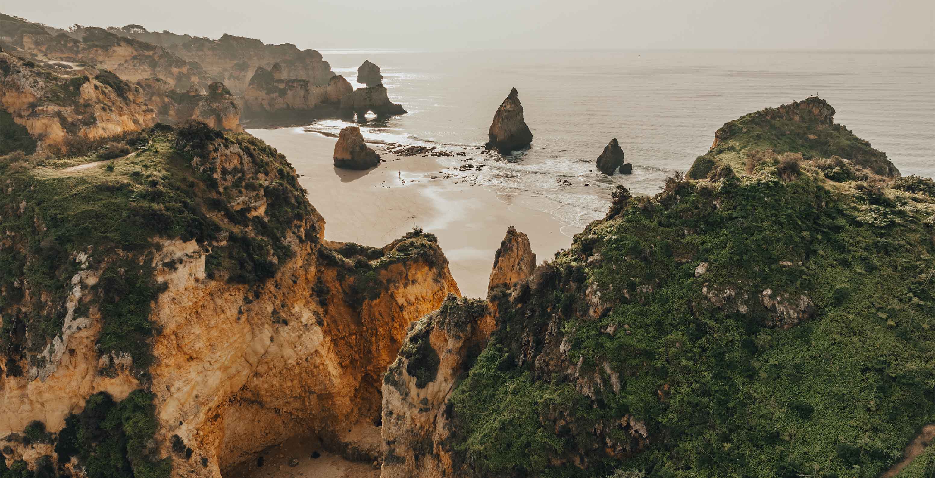 Vista desde arriba de la playa de los Tres Hermanos, con formaciones rocosas y vegetación, hacia el mar con niebla