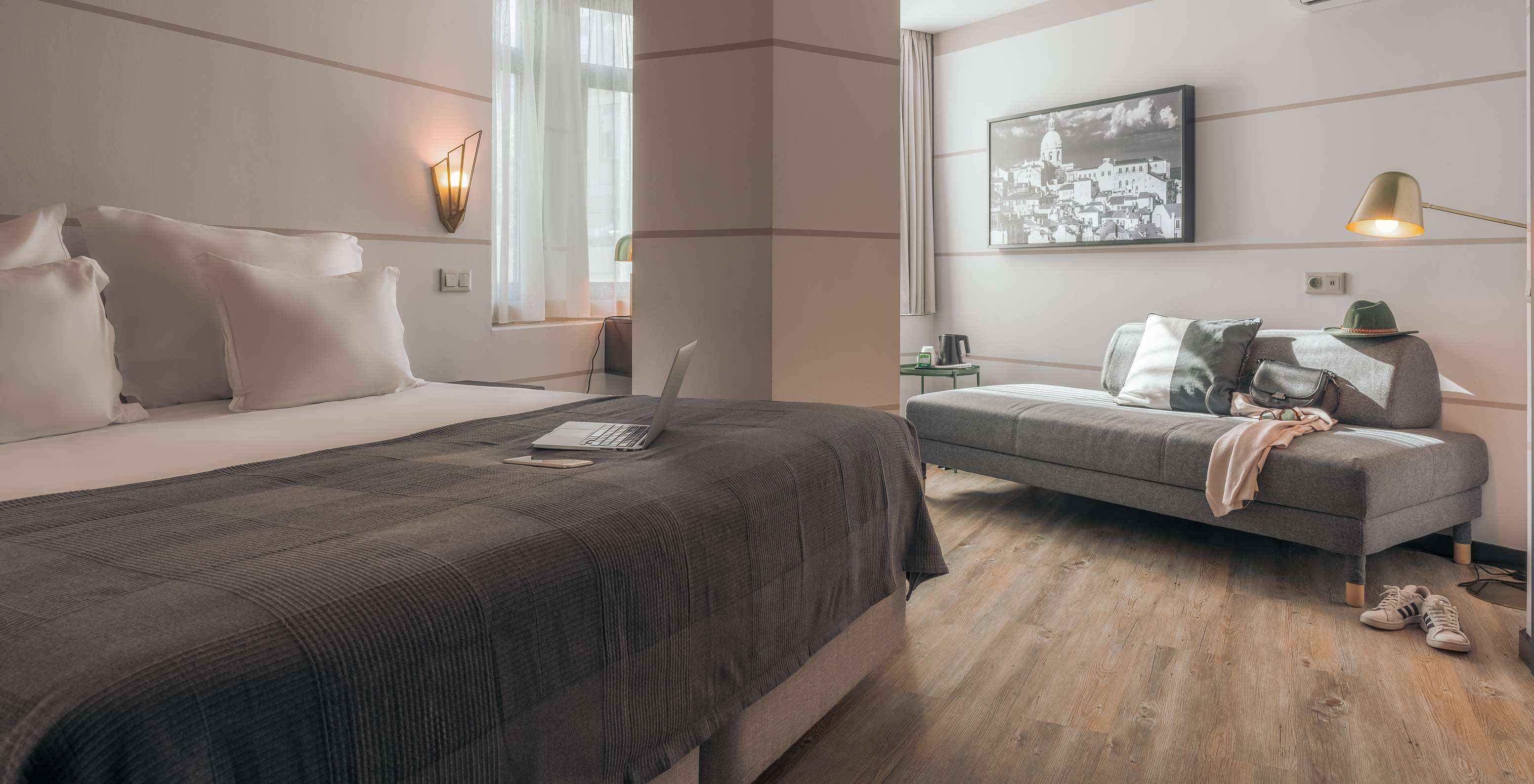 El Double Superior del Pestana Lisboa Vintage tiene una cama matrimonial con manta gris, un sofá gris y unos tenis blancos