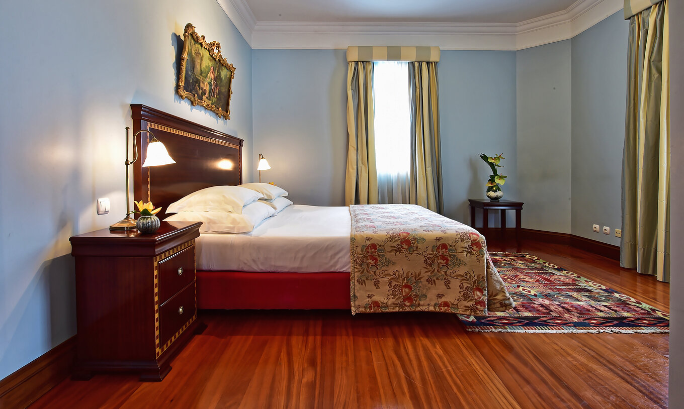 La Suite Miramar del Pestana Miramar tiene una cama matrimonial con una colcha de flores y una mesa de noche de madera oscura