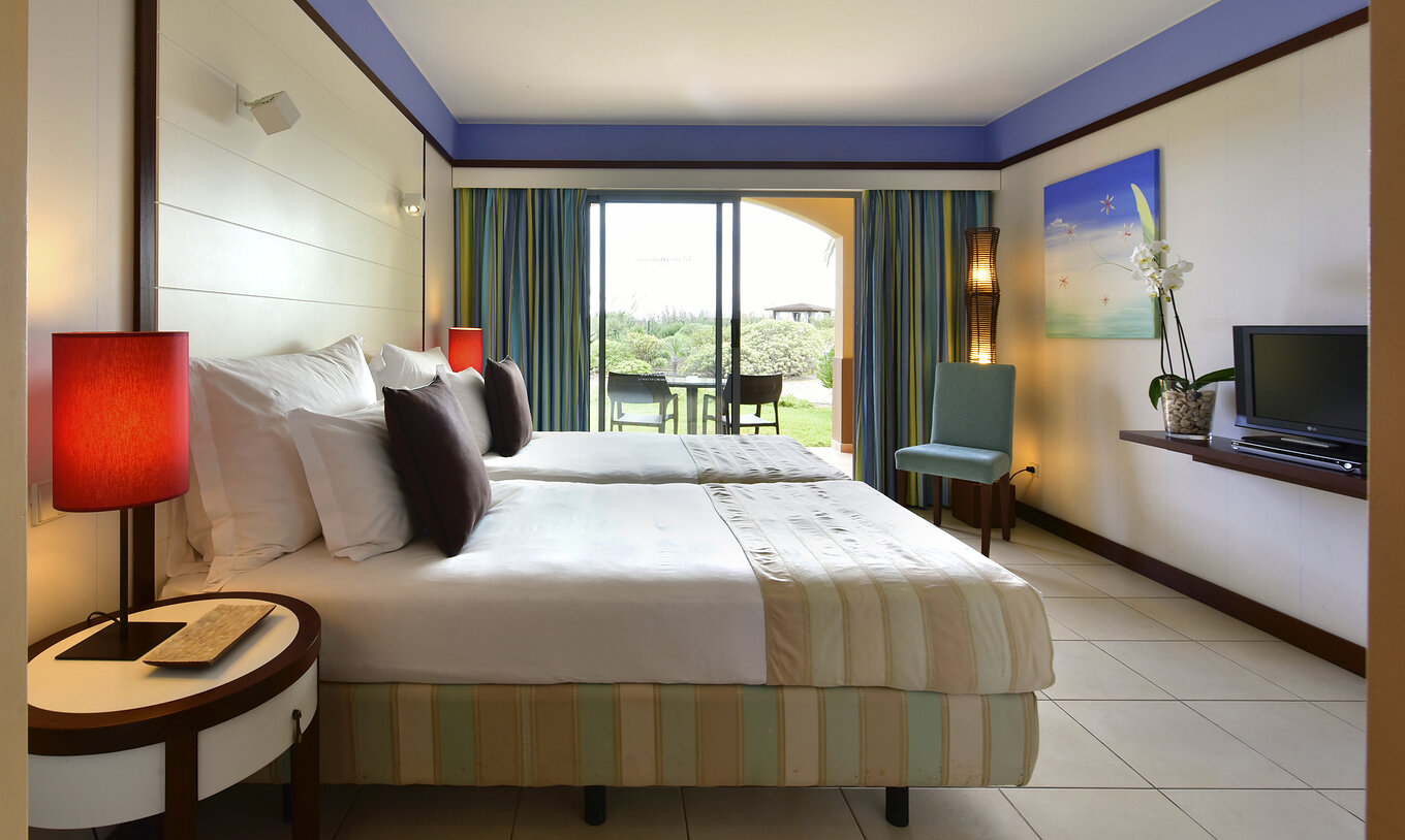 El Doble Clásico del Pestana Porto Santo All Inclusive tiene dos camas, una silla y un balcón con una mesa y vista al jardín