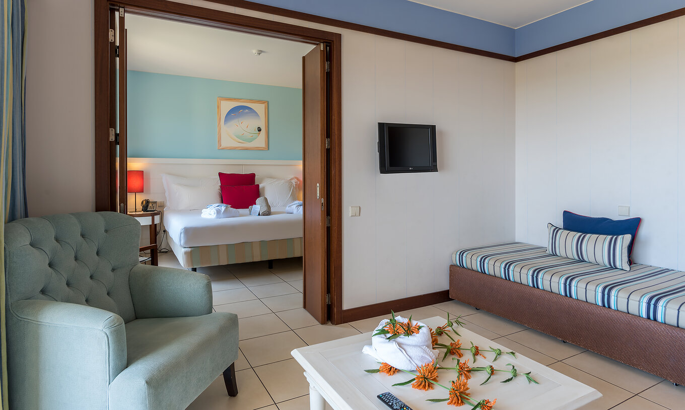 La Suite Apartamento T1 del Pestana Porto Santo All Inclusive tiene un cuarto con cama y una sala con sofá y televisión