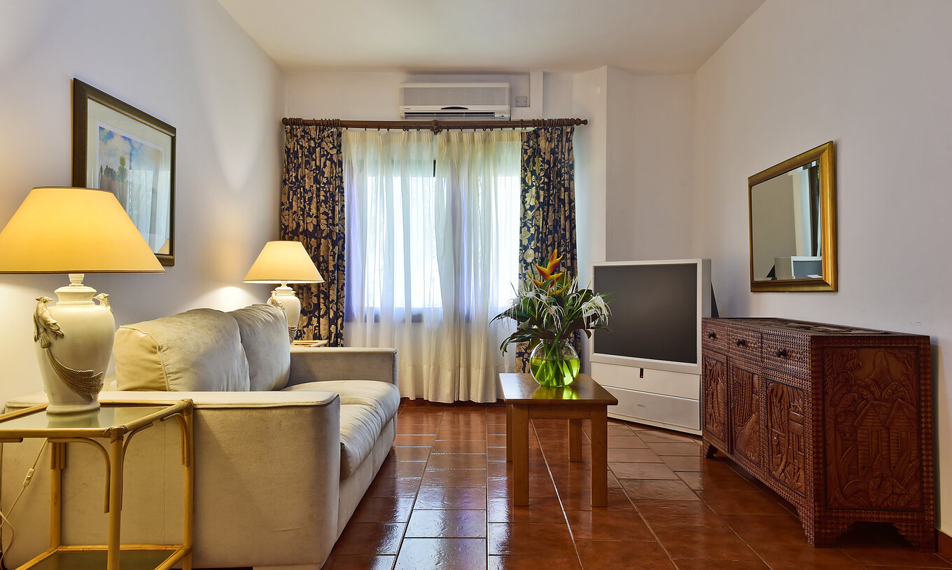 La Suite del Pestana Miramar São Tomé tiene una sala de estar con sofá, televisor y una mesa con un jarrón de flores