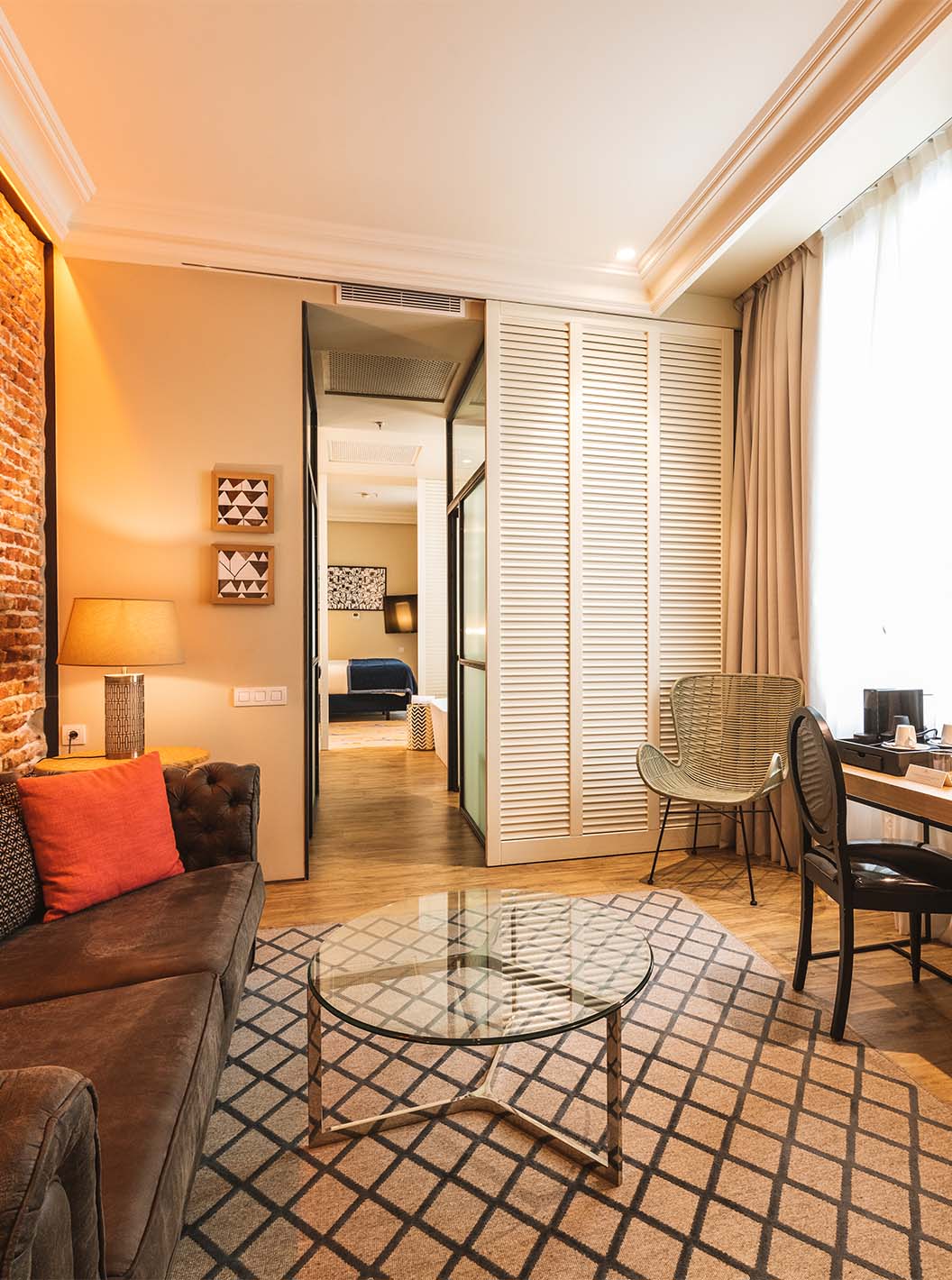 La Suite del Pestana Plaza Mayor Madrid tiene una sala de estar con escritorio, sofá, televisión y una pared de ladrillo