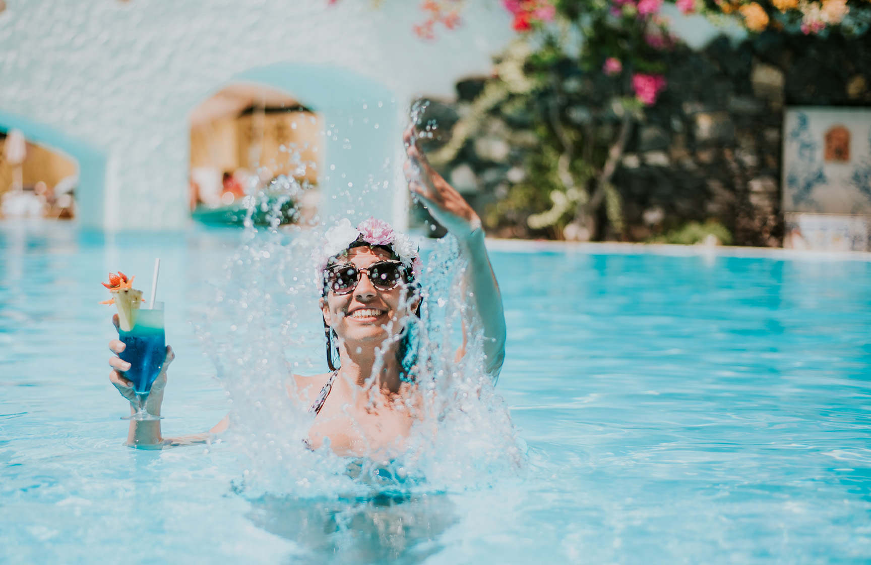 Mujer feliz jugando con el agua, con un cóctel en la mano, disfrutando del paquete todo incluido sin preocupaciones