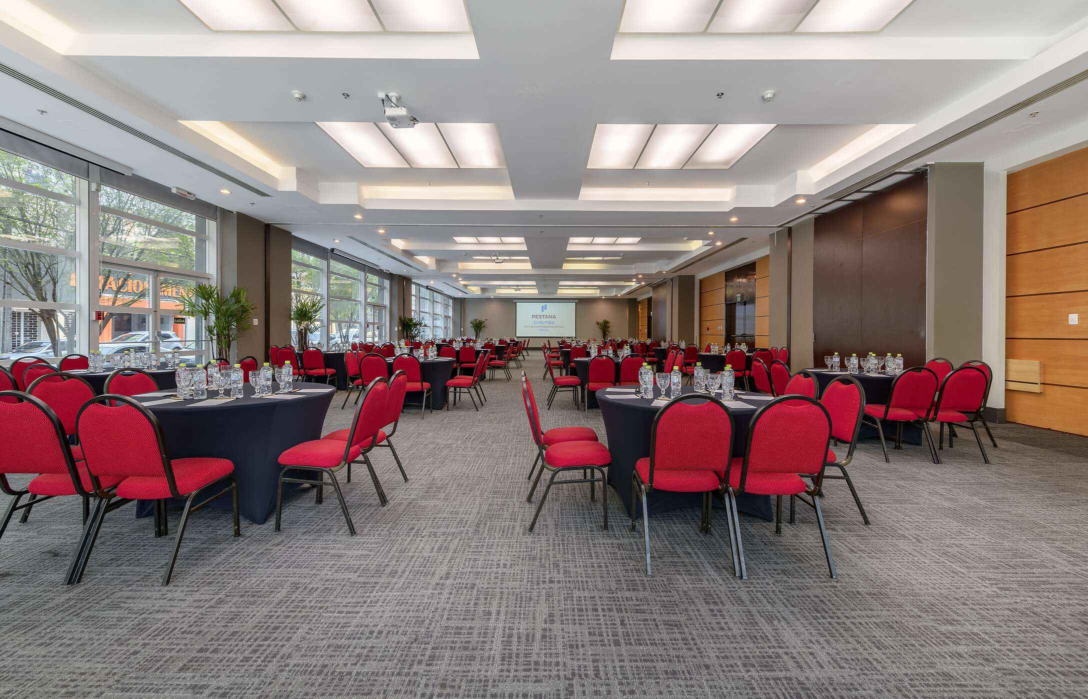 Sala para reuniones o conferencias, con varias mesas redondas, sillas rojas, copas y botellas de agua