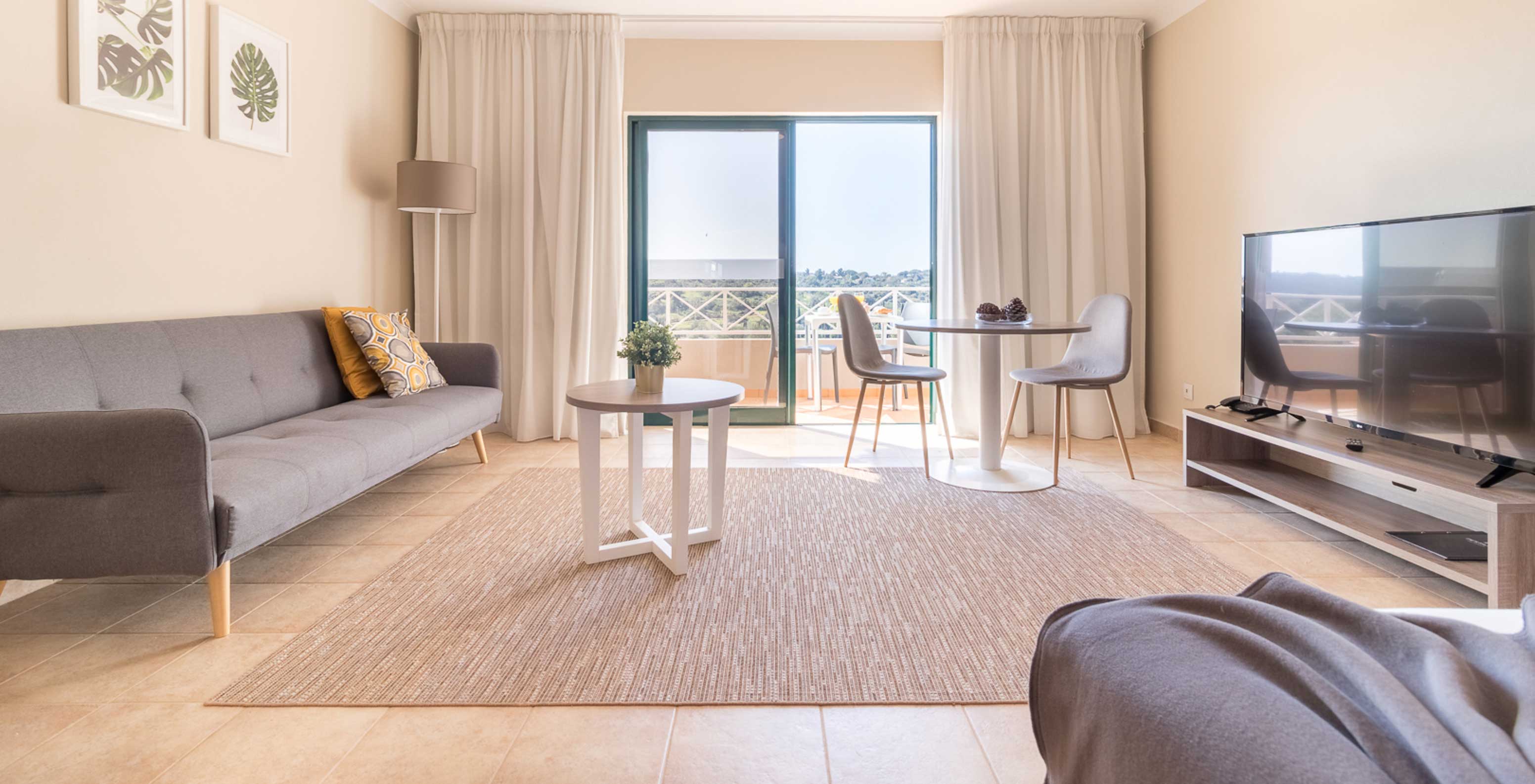 De studio van Pestana Gramacho Residences heeft een zitkamer met grijze bank, tv, tafel en helder balkon