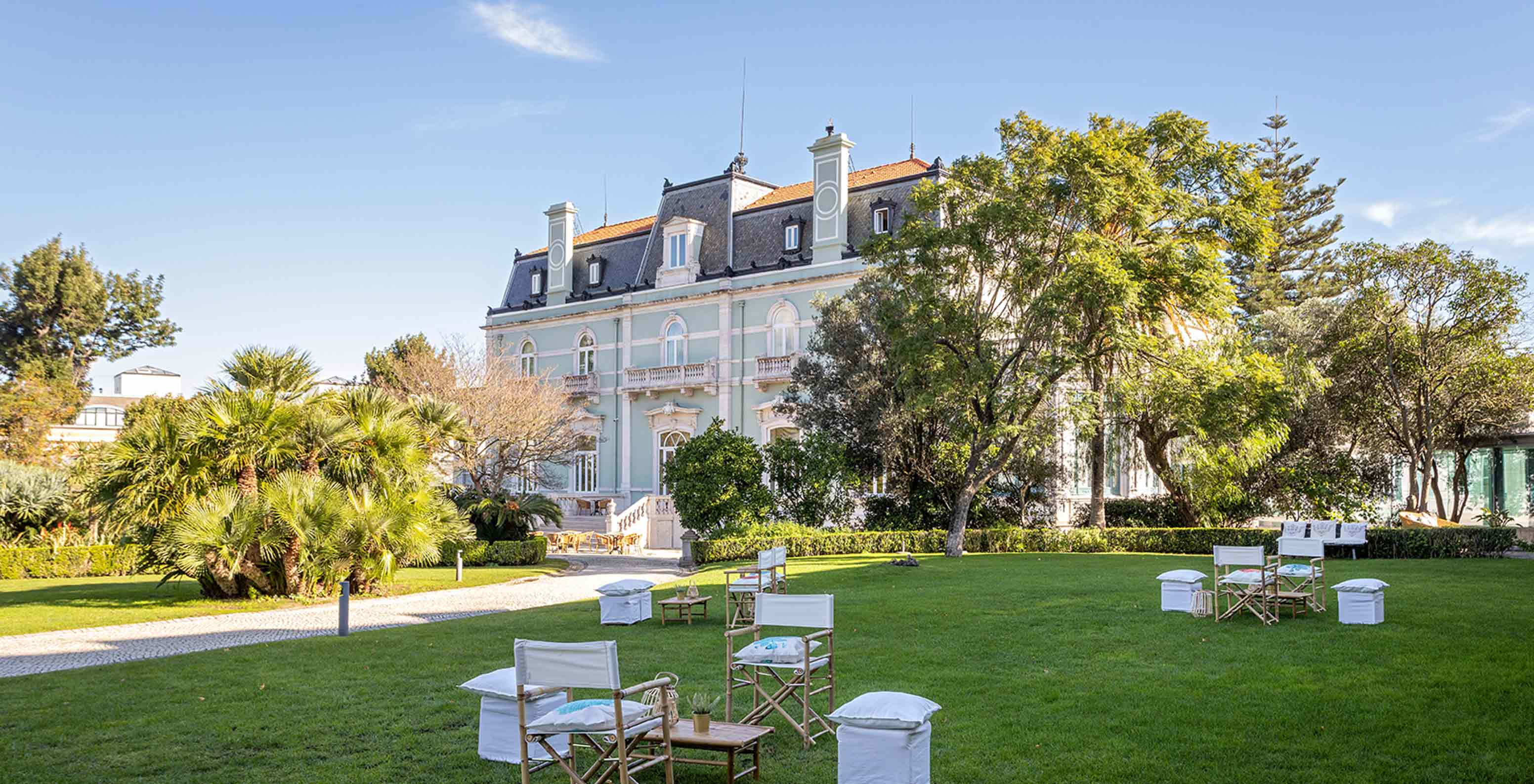 Pestana Palace Lisboa heeft een tuin met tafels en stoelen op groen gras, dicht bij het hoofdgebouw	