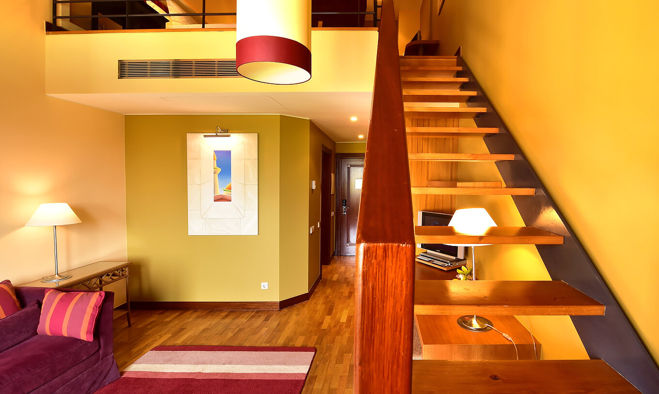 De Mezzanine Jacuzzi Suite van Pestana Sintra Golf heeft een bank, trap naar de mezzanine, schilderij en een lamp