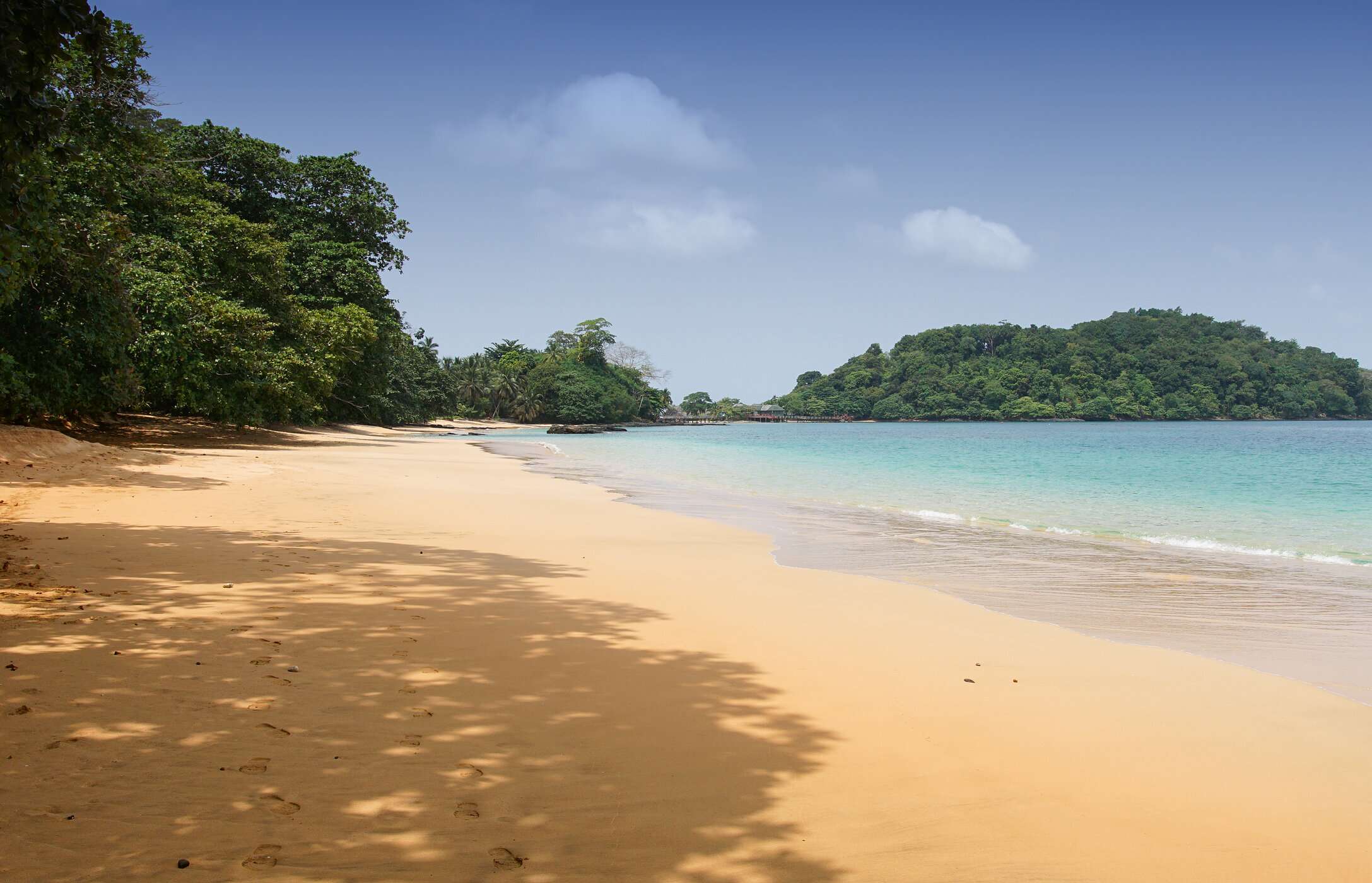 Uitzicht op Coco Beach in São Tomé en Príncipe, met gouden zand, kalm kristalhelder water en omringende vegetatie.