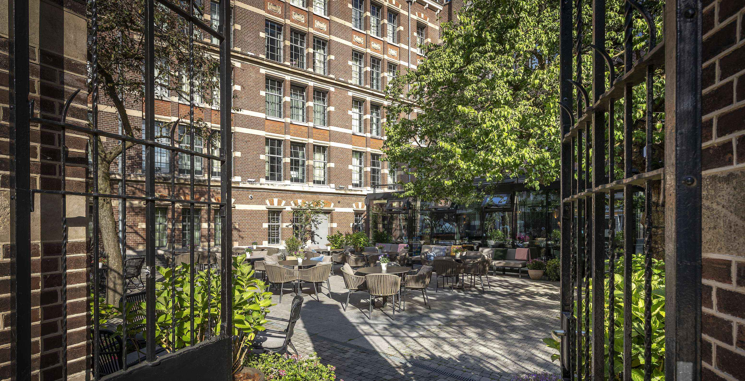 Terras van Pestana Amsterdam Riverside, met ronde tafels en stoelen, met de gevel van het hotel op de achtergrond