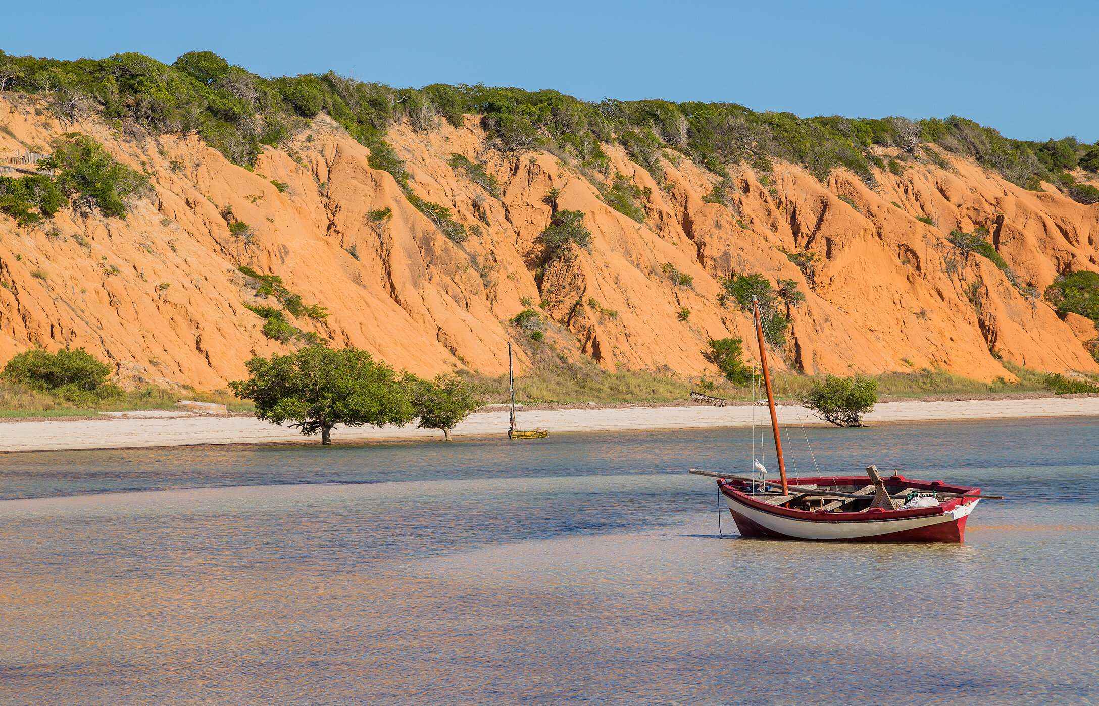 Vista do mar, da ilha de Magaruque com um barco tradicional ancorado e falésias avermelhadas no fundo