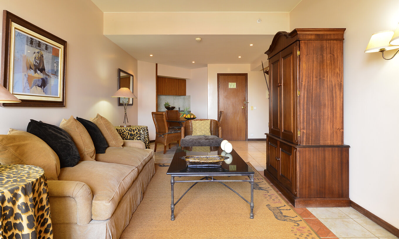 A Suite Luxo do Pestana Rovuma tem uma sala com um sofá branco em bege e duas mesas com toalhas leopardo