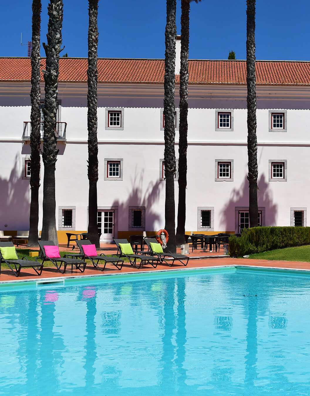 Piscina exterior da Pousada Convento Beja, um hotel histórico no Alentejo, com várias espreguiçadeiras com almofadas