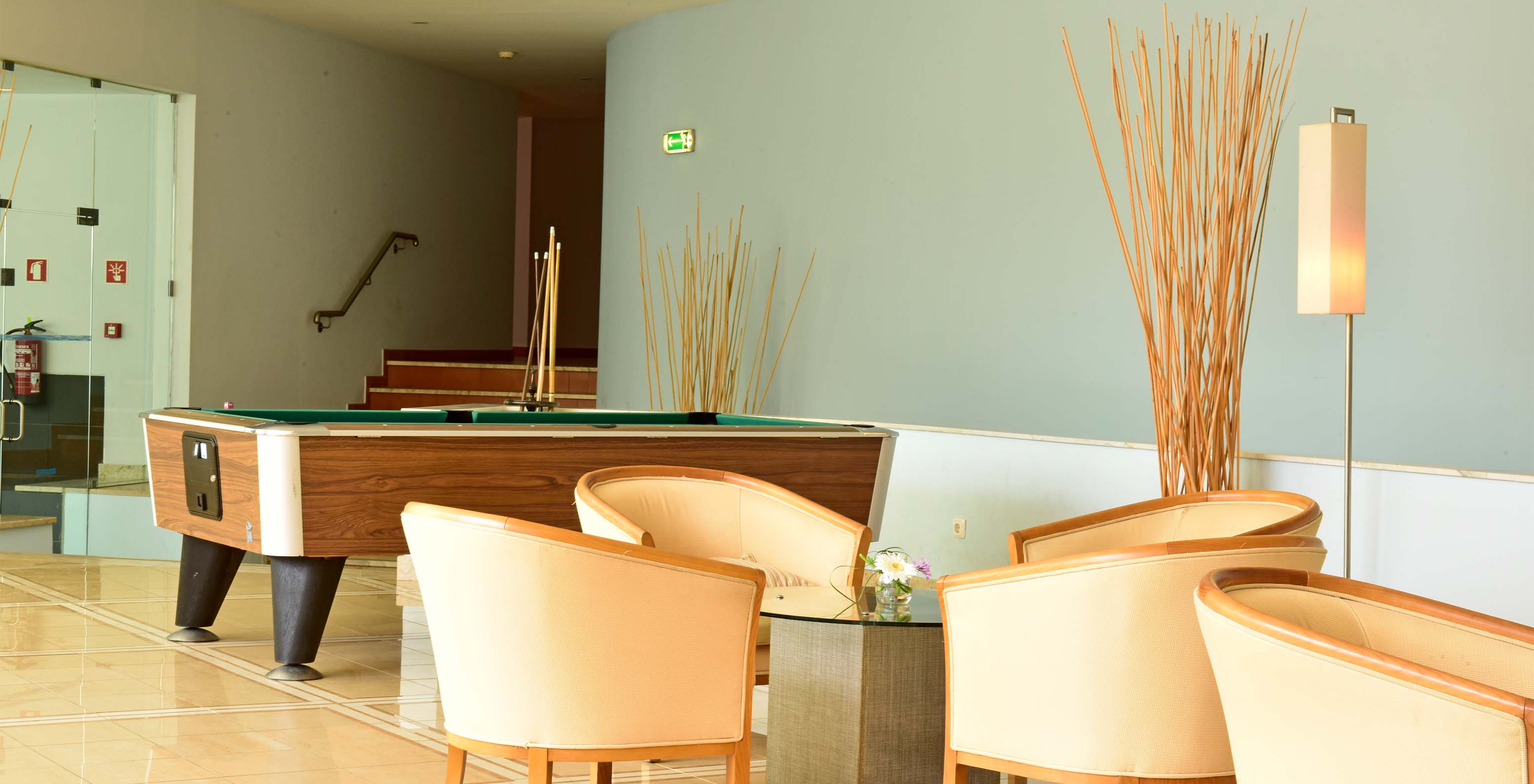 Sala de jogos com mesa de snooker, cadeiras e mesa de apoio central, com escadas no fundo e decoração