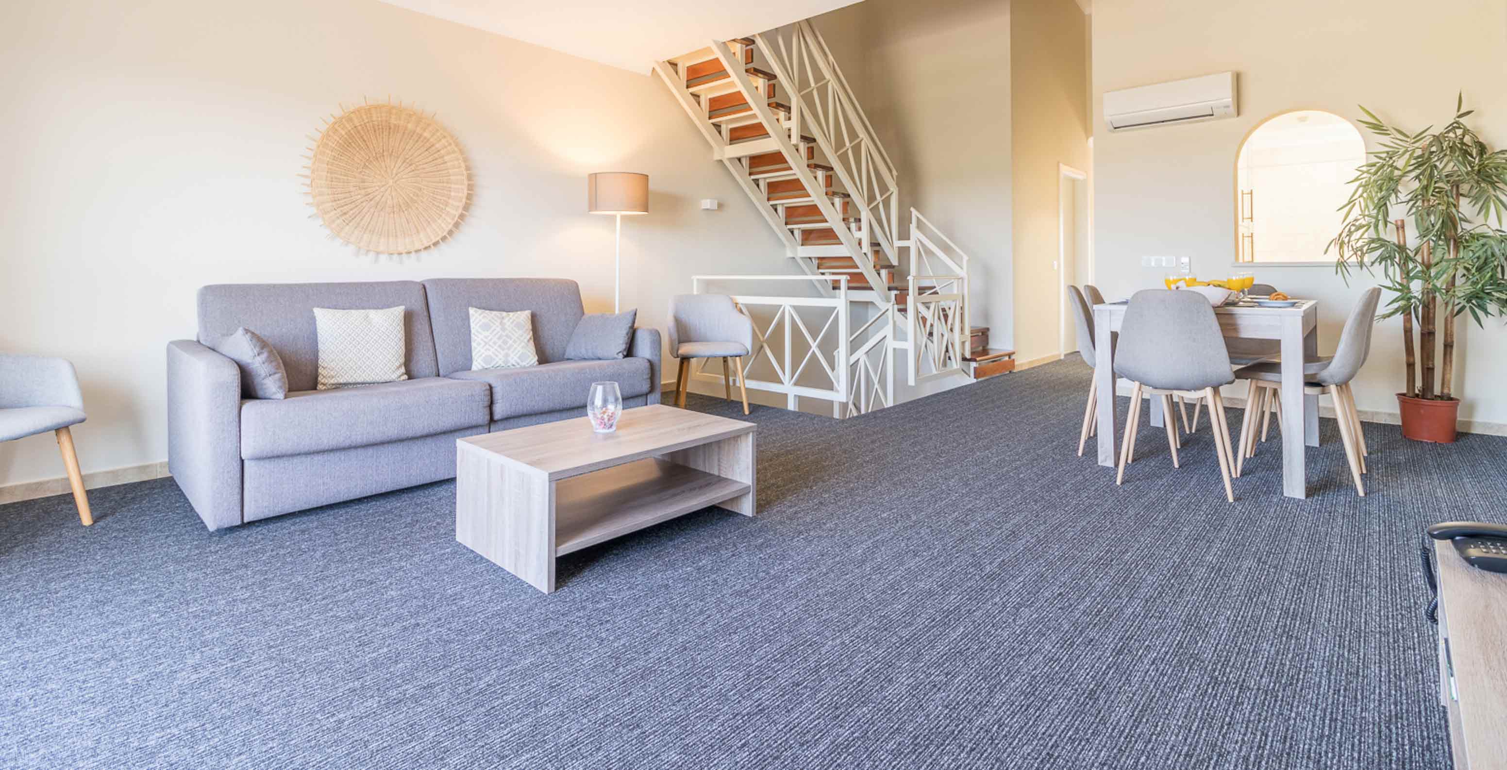 O Apartamento T2 do Pestana Gramacho Residences tem uma sala de estar com um sofá cinzento, mesa de centro e escadas ao fundo