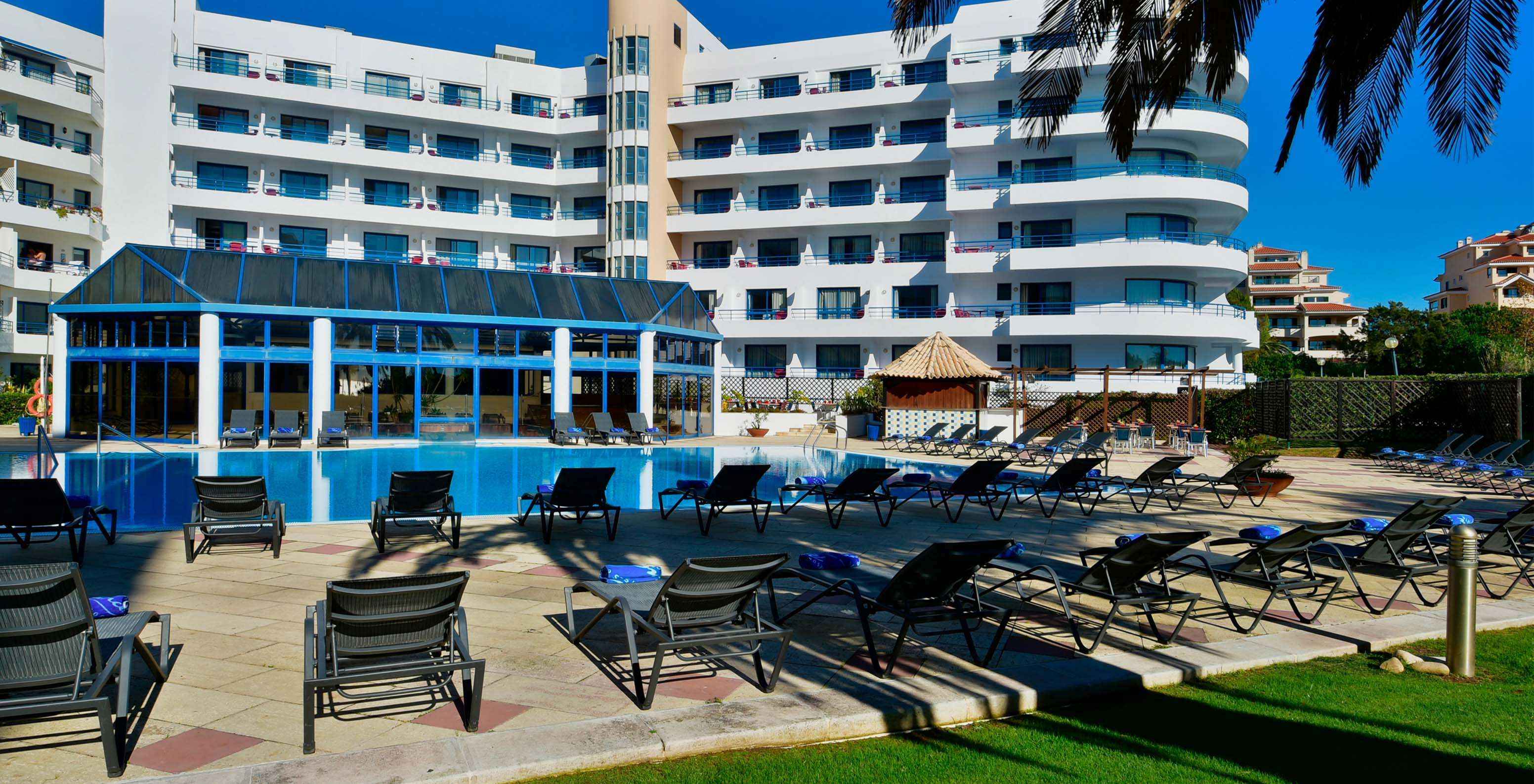 Vista do jardim do Pestana Cascais para a piscina exterior, espreguiçadeiras, e o bar da piscina